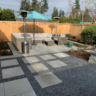 Small residential backyard with rock paver patio and custom garden beds and wood fencing in Seattle, Washington neighborhood.