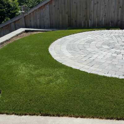 Dream turf encircles a round paver patio in small Seattle backyard.
