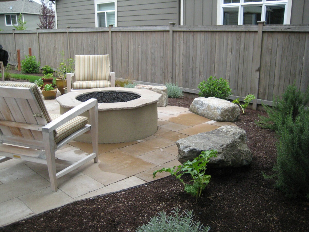 Backyard landscaping with custom rock fire pit, paver patio and hardscaping with lush plants native to the Pacific Northwest.