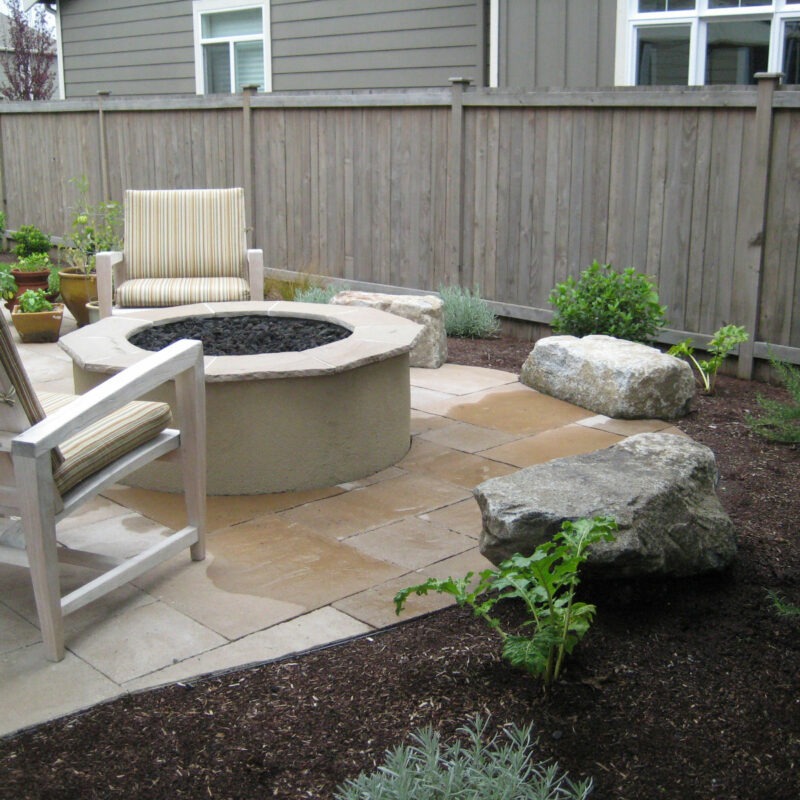 Backyard landscaping with custom rock fire pit, paver patio and hardscaping with lush plants native to the Pacific Northwest.
