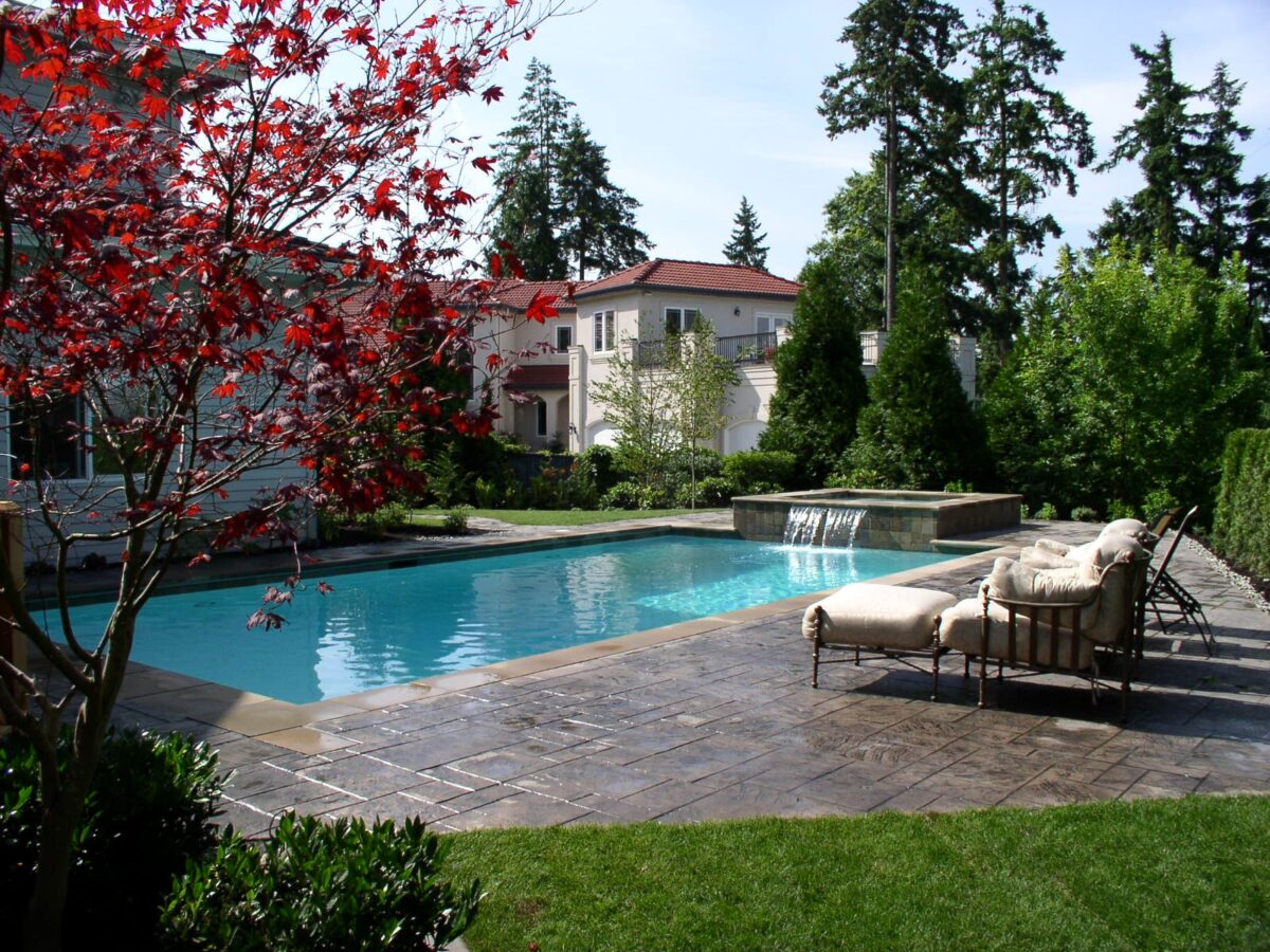 Large blue pool with paver patio has a waterfall feature from the hot tub to the pool at Seattle residence.