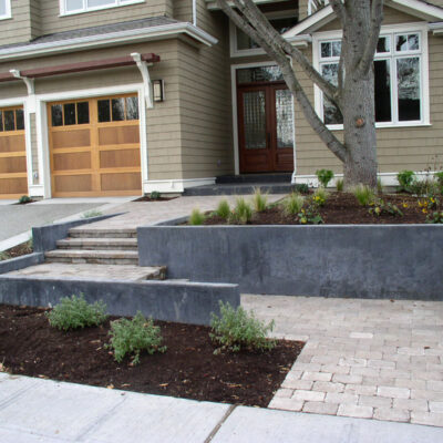 A black concrete retaining wall with paver walking path and steps creates a modern entryway for this Seattle homeowner.