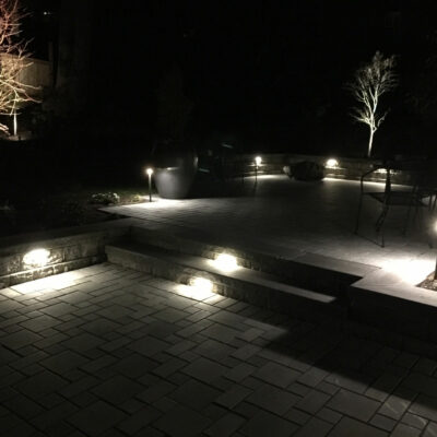 Backyard paver patio seen at night is illuminated with custom outdoor lighting from Lifestyle Landscapes located in Seattle, Washington.
