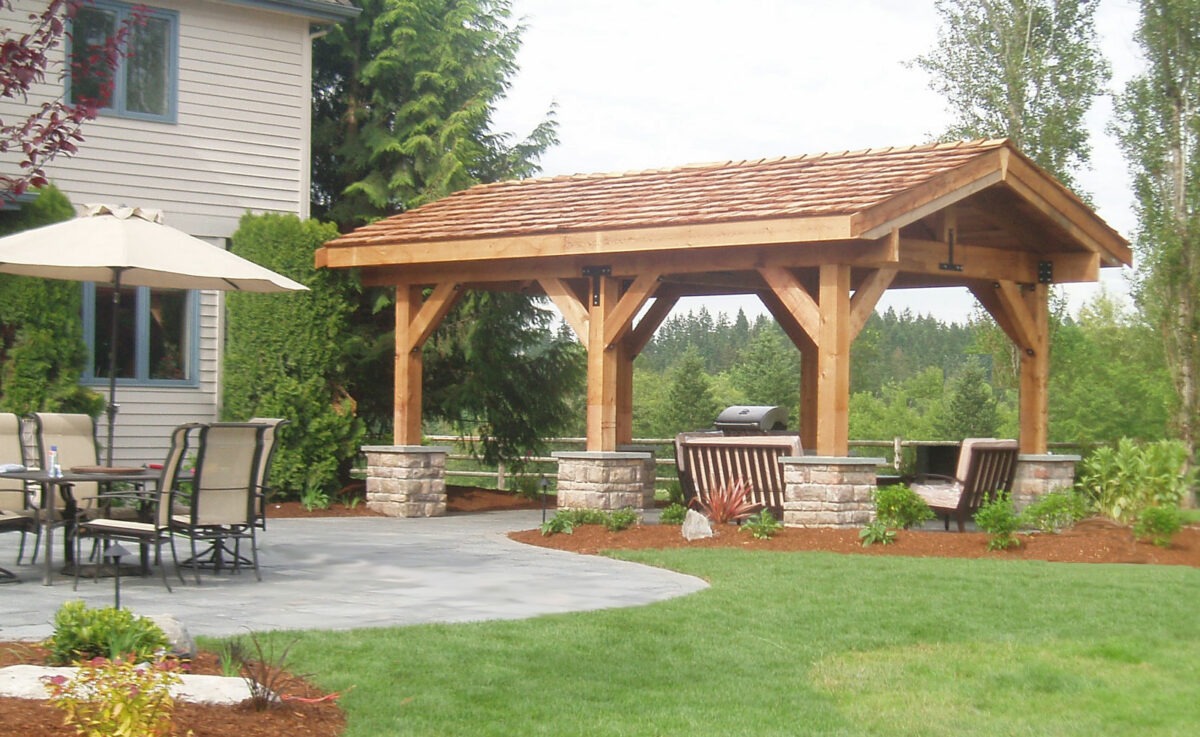 This large outdoor pavilion covers a custom paver patio and bbq pit in Seattle, Washington backyard.