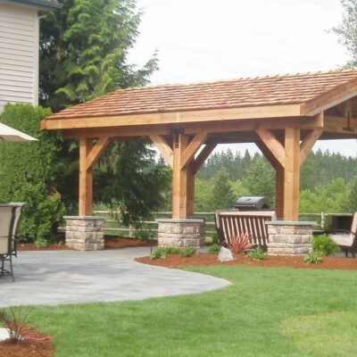 This large outdoor pavilion covers a custom paver patio and bbq pit in Seattle, Washington backyard.