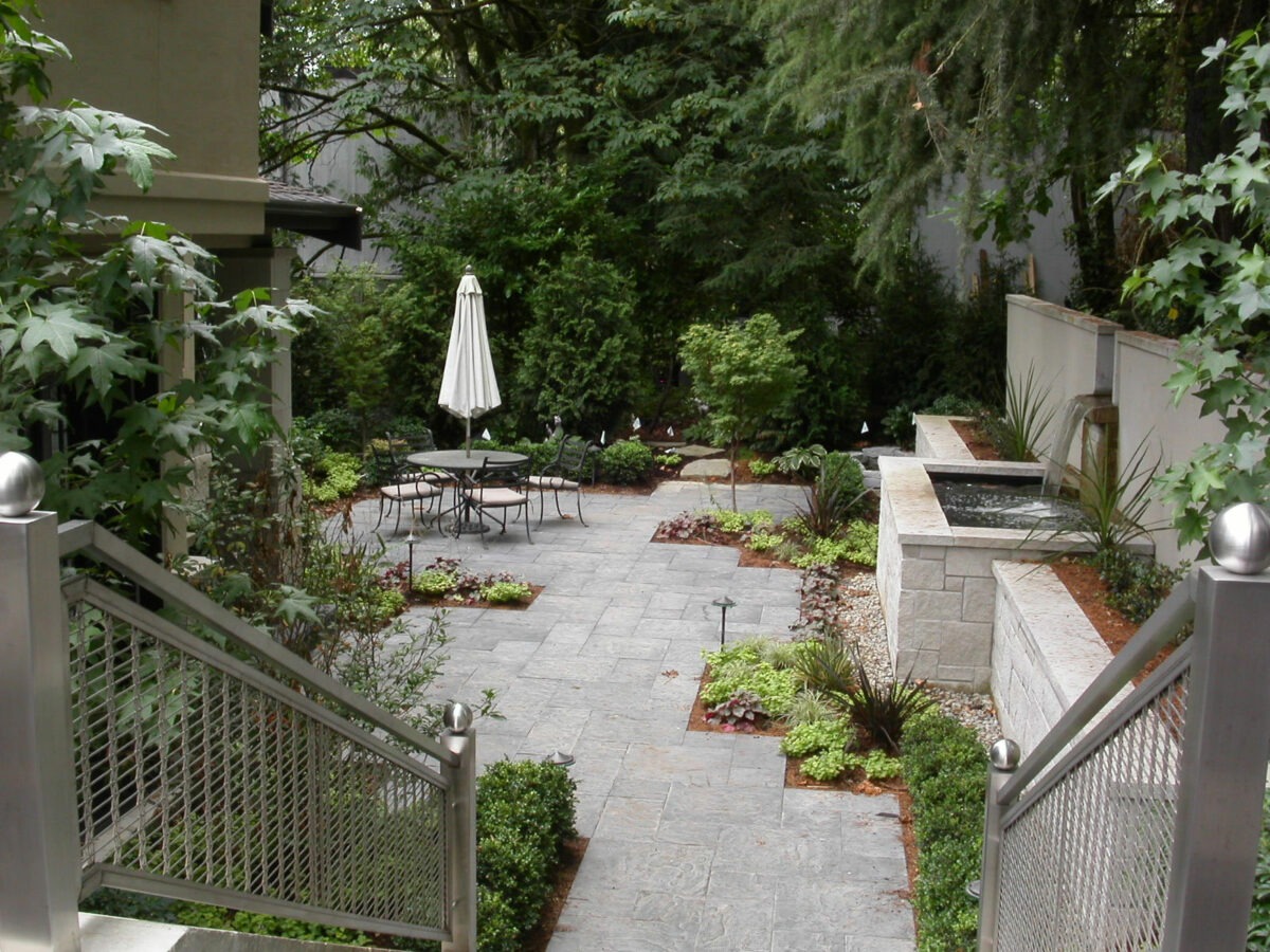 Large Seattle backyard patio with large retaining wall boasts a water fountain and paver patio with luxury landscaping by Lifestyle Landscapes.