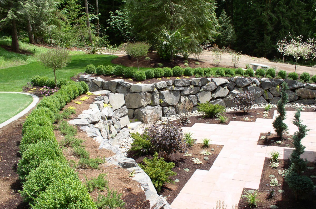 Large boulder rock retaining wall divides this backyard between the patio and the steep incline to the backyard of Seattle home.