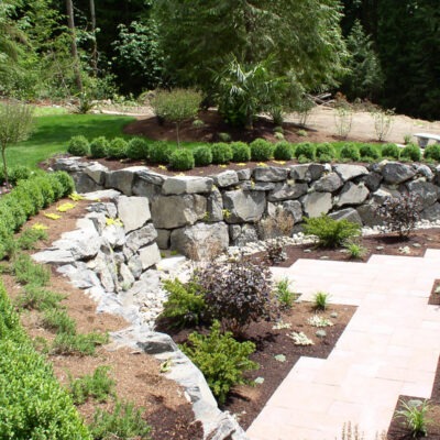 Large boulder rock retaining wall divides this backyard between the patio and the steep incline to the backyard of Seattle home.
